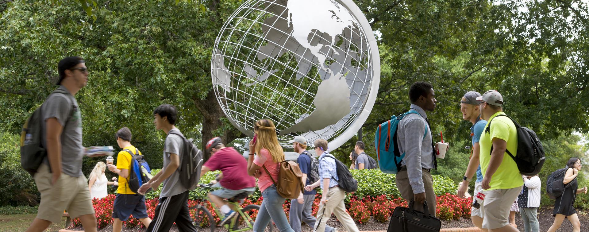 Picture of students on campus walking past a large statue of a globe. 